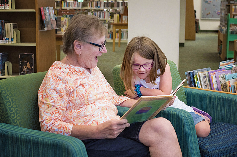 A woman reads a book to her grandchild at the library.