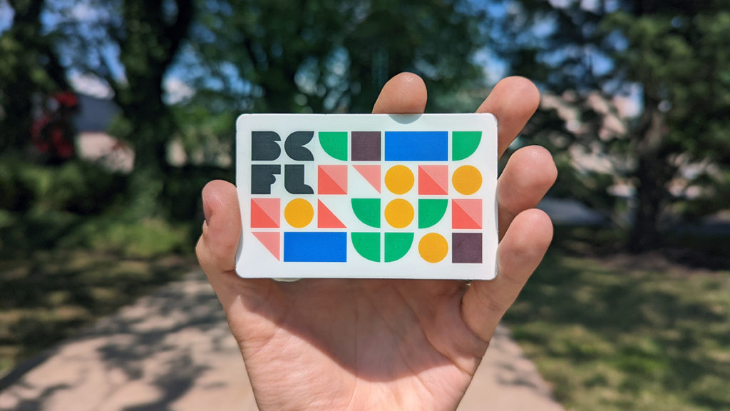 A photo of a hand holding a Bucks County Free Library card outside the Doylestown branch of the library